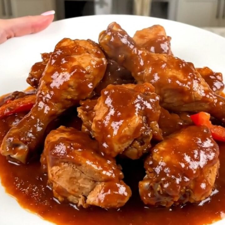 A black slow cooker filled with chicken thighs, colorful bell peppers, onions, and a rich tomato sauce.
