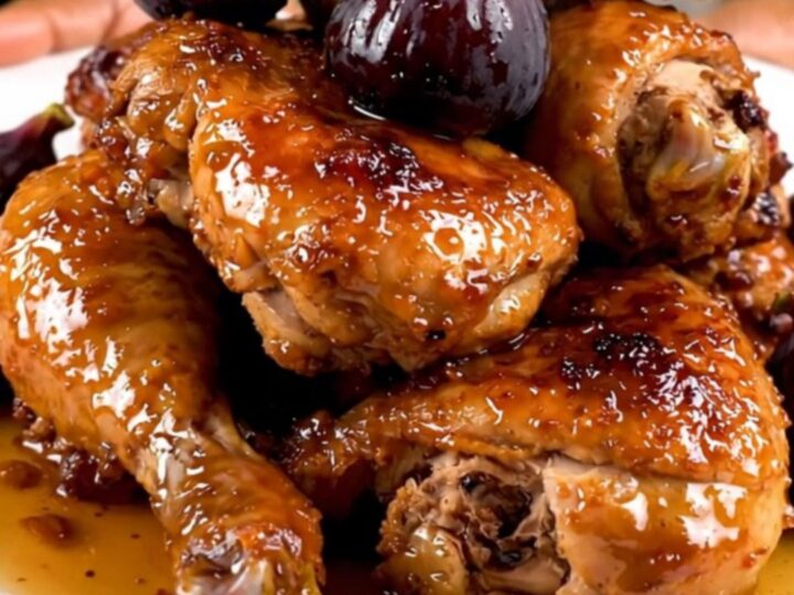 A close-up shot of slow-cooked chicken thighs with figs and onions on a white plate.