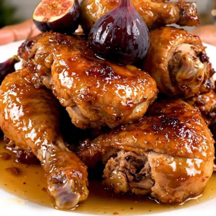 A close-up shot of slow-cooked chicken thighs with figs and onions on a white plate.