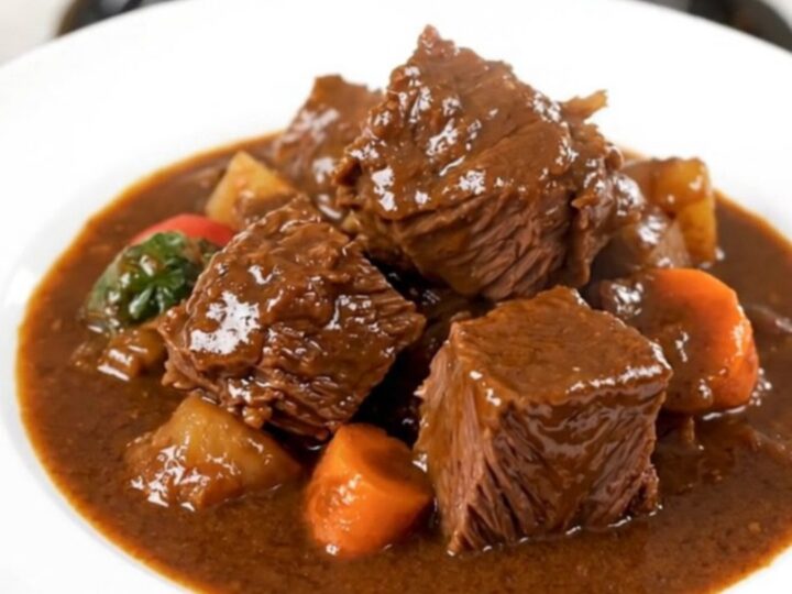 A steaming bowl of red wine beef stew with tender beef cubes and bright orange carrot slices in a rich dark sauce.