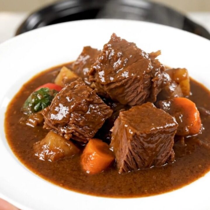 A steaming bowl of red wine beef stew with tender beef cubes and bright orange carrot slices in a rich dark sauce.