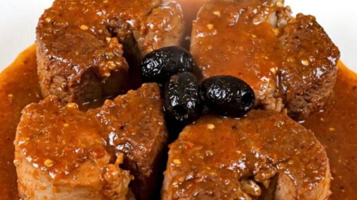 A rustic bowl of tender slow-cooked pork cheeks in a rich tomato sauce with black olives.