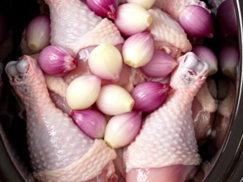 A close-up of tender chicken thighs covered in a glossy red wine glaze with whole shallots on a white plate.
