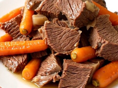 A rustic slow cooker filled with tender braised beef chuck, whole carrots, and halved turnips in a rich broth.