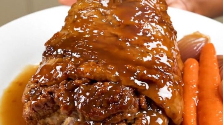A slow-cooked, tender pork shank served on a white plate with glazed shallots and carrots.