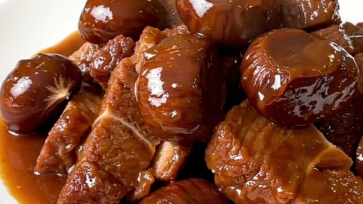 A close-up of tender pork collar chunks and whole chestnuts in a rich brown sauce served on a white plate.