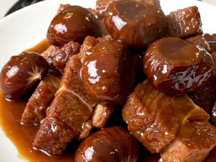 A close-up of tender pork collar chunks and whole chestnuts in a rich brown sauce served on a white plate.