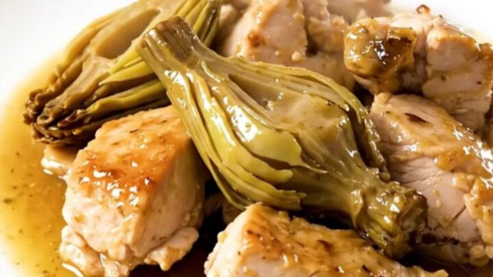 A close-up of tender chicken pieces and artichoke hearts coated in a glossy, light wine sauce in a slow cooker.