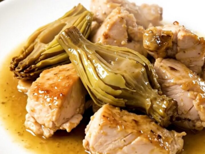 A close-up of tender chicken pieces and artichoke hearts coated in a glossy, light wine sauce in a slow cooker.