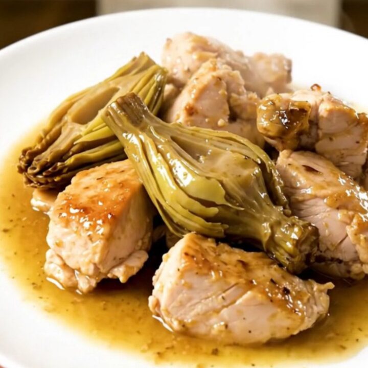 A close-up of tender chicken pieces and artichoke hearts coated in a glossy, light wine sauce in a slow cooker.