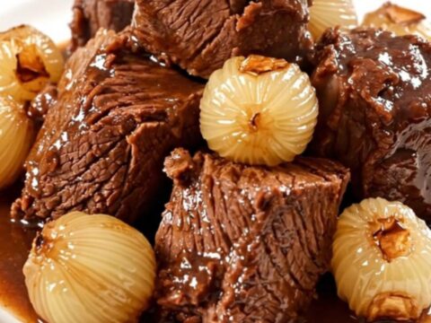Bœuf braisé fondant servi dans une assiette blanche avec ses oignons grelots.