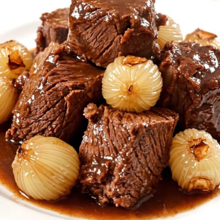 Bœuf braisé fondant servi dans une assiette blanche avec ses oignons grelots.