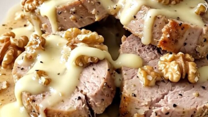 A ceramic slow cooker filled with raw pork tenderloin, slices of brie, crushed walnuts, and heavy cream.