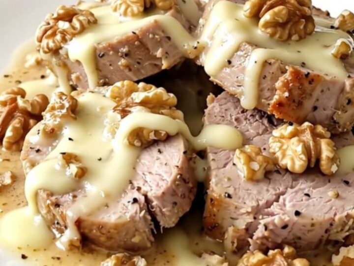 A ceramic slow cooker filled with raw pork tenderloin, slices of brie, crushed walnuts, and heavy cream.