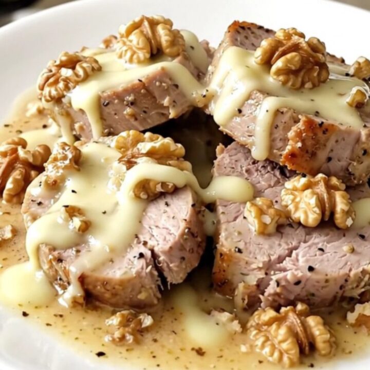 A ceramic slow cooker filled with raw pork tenderloin, slices of brie, crushed walnuts, and heavy cream.