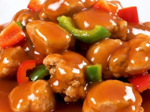 A slow cooker filled with chicken, pineapple, and red bell peppers in a glossy sweet and sour sauce.