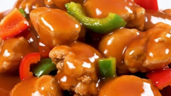 A slow cooker filled with chicken, pineapple, and red bell peppers in a glossy sweet and sour sauce.