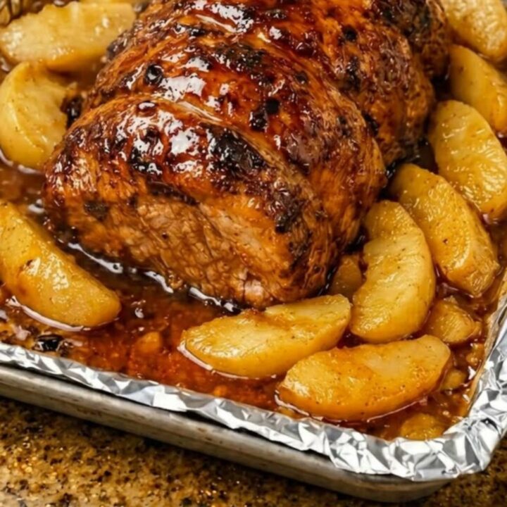 A glistening honey garlic apple pork roast served on a tray with caramelized apple wedges.