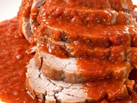 A slow-cooked pork roast covered in rich red tomato sauce served on a white plate.