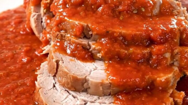 A slow-cooked pork roast covered in rich red tomato sauce served on a white plate.