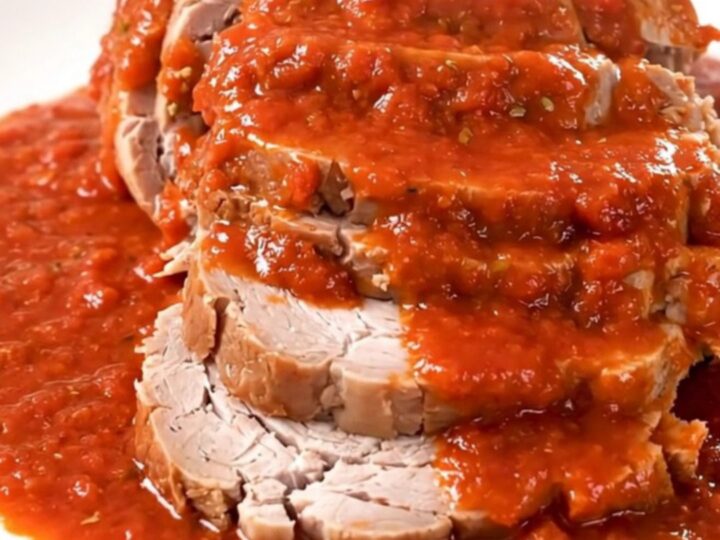 A slow-cooked pork roast covered in rich red tomato sauce served on a white plate.