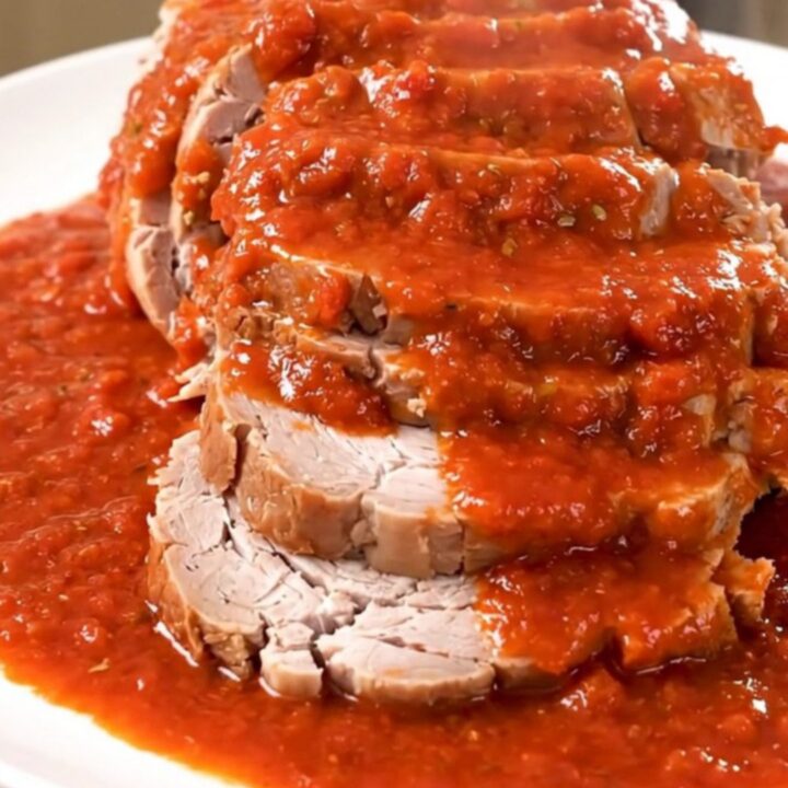 A slow-cooked pork roast covered in rich red tomato sauce served on a white plate.