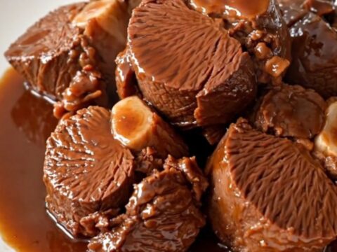 Close up of tender braised beef cheeks in a rich red wine sauce with whole shallots.