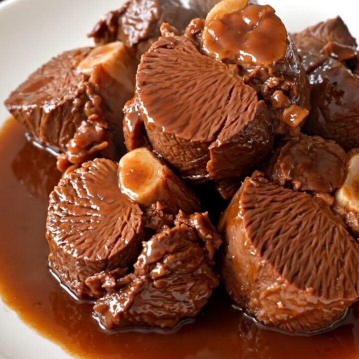 Close up of tender braised beef cheeks in a rich red wine sauce with whole shallots.
