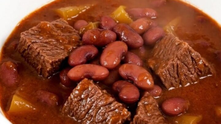 A steaming bowl of beef and red bean stew in a white bowl on a wooden table.