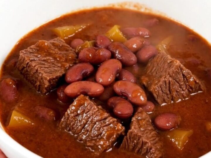 A steaming bowl of beef and red bean stew in a white bowl on a wooden table.