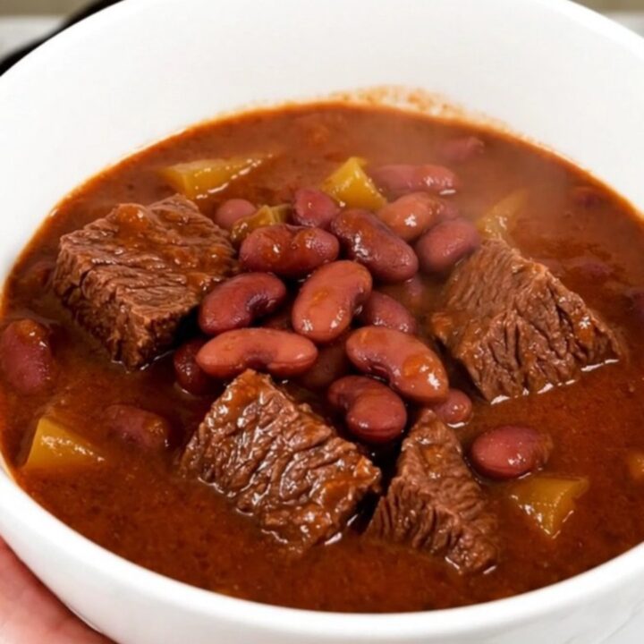 A steaming bowl of beef and red bean stew in a white bowl on a wooden table.
