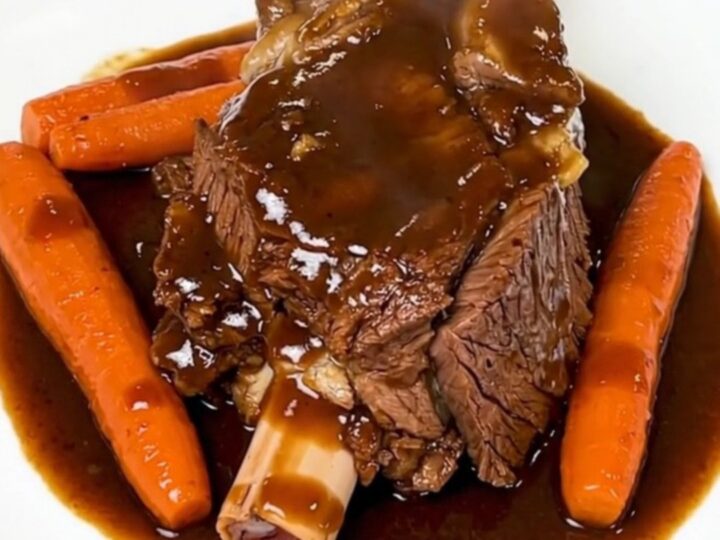 A rustic plate featuring a tender, slow-cooked beef shank with glossy, soft carrots in a rich, red wine sauce.