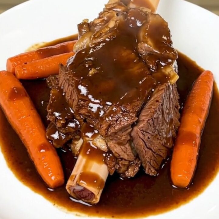 A rustic plate featuring a tender, slow-cooked beef shank with glossy, soft carrots in a rich, red wine sauce.