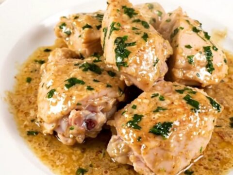 A top-down view of a black slow cooker filled with raw chicken thighs, sliced leeks, and wheat beer.