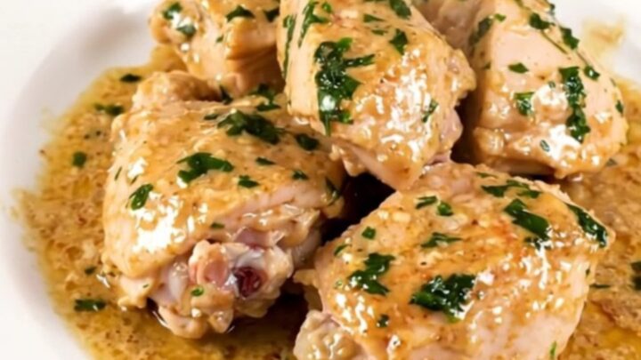A top-down view of a black slow cooker filled with raw chicken thighs, sliced leeks, and wheat beer.