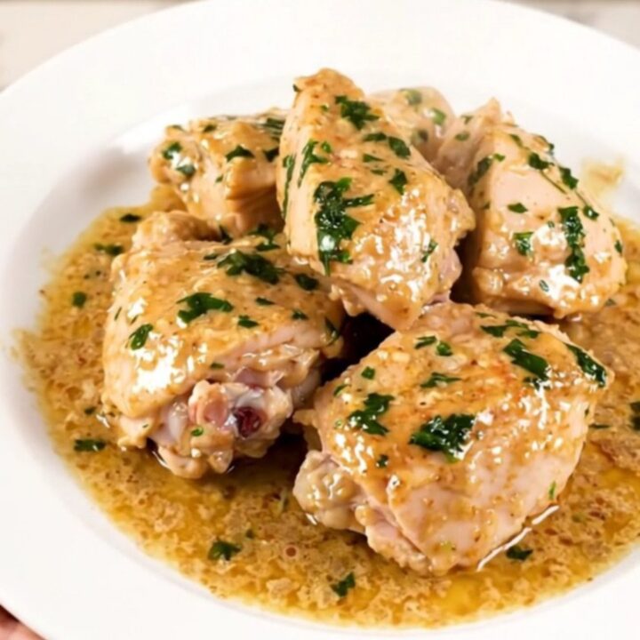 A top-down view of a black slow cooker filled with raw chicken thighs, sliced leeks, and wheat beer.