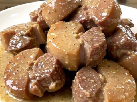 A close-up of tender pork cheeks in a creamy leek sauce served on a white plate.