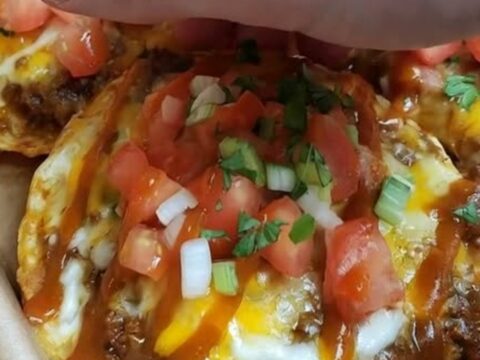 A crispy Mexican pizza topped with melted cheese, red sauce, fresh diced tomatoes, and sliced green onions.