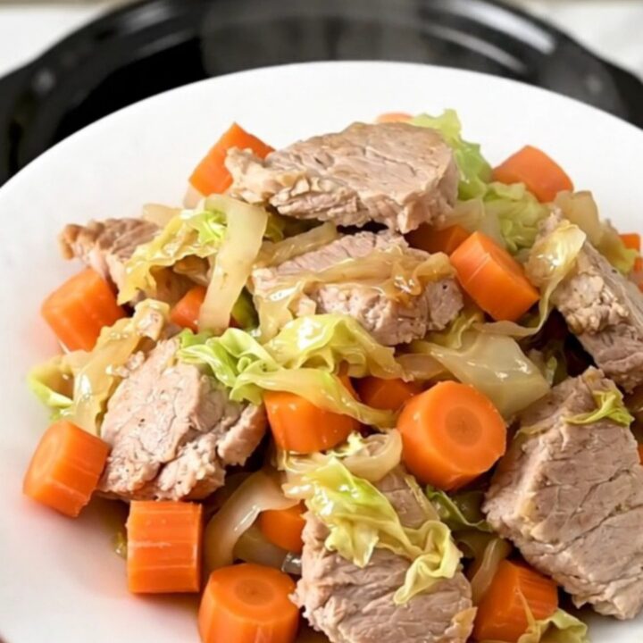 Échine de porc fondante avec des carottes et du chou dans une mijoteuse noire.