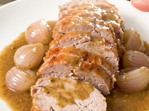A top-down view of a raw pork tenderloin in a slow cooker with shallots and herbs.