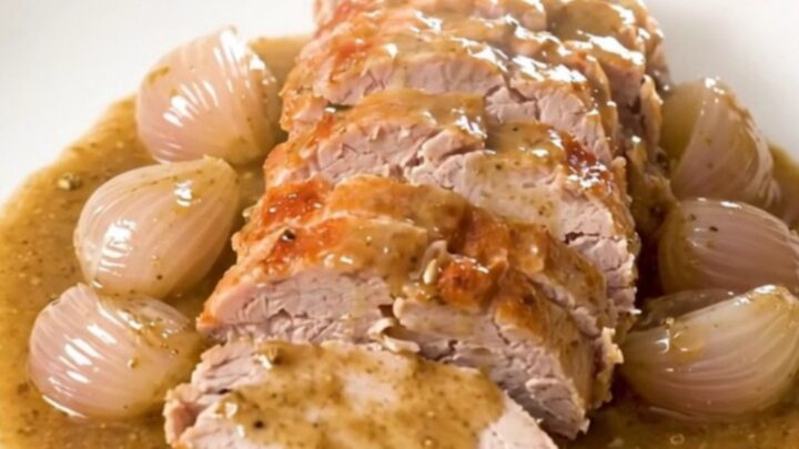 A top-down view of a raw pork tenderloin in a slow cooker with shallots and herbs.