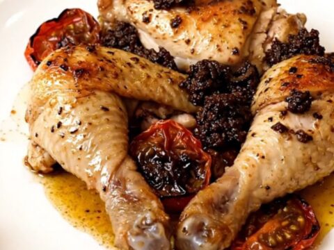 Slow cooker filled with cooked chicken breasts topped with cherry tomatoes and black tapenade.