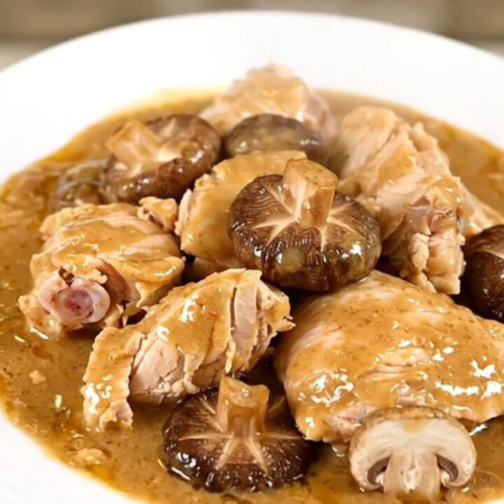 A top-down view of a slow cooker filled with raw chicken thighs, sliced shiitake mushrooms, and broth.