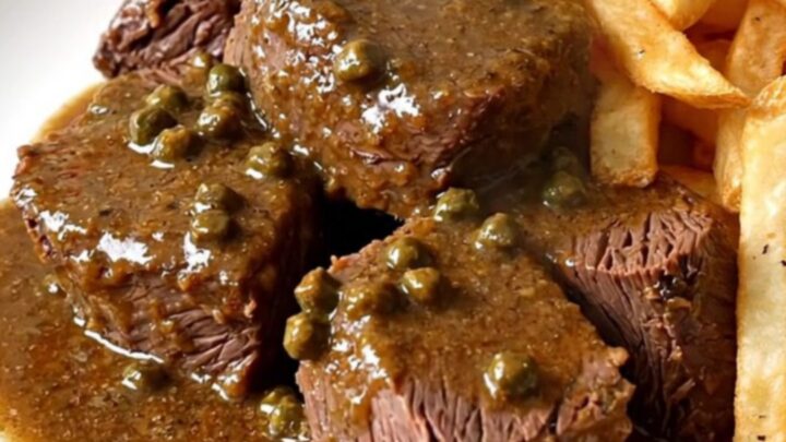A close-up of tender braised pepper beef served on a white plate with golden fries.