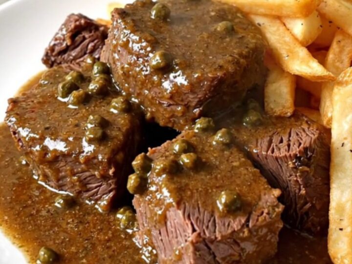 A close-up of tender braised pepper beef served on a white plate with golden fries.