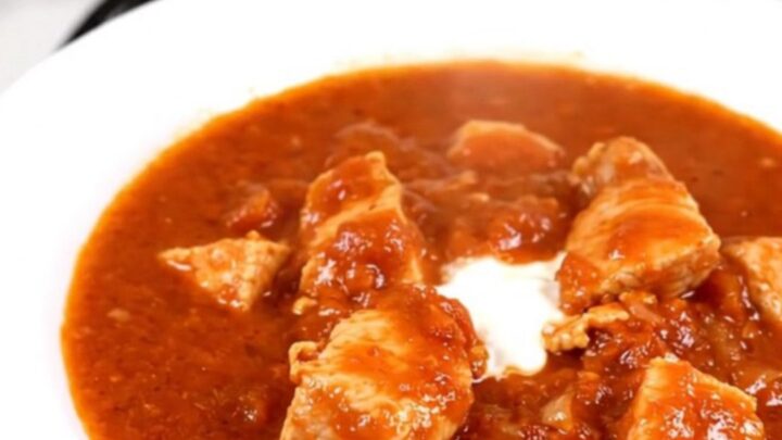 A steaming, glossy portion of chicken goulash served on a white round plate.