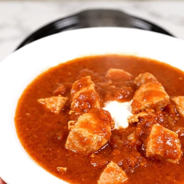 A steaming, glossy portion of chicken goulash served on a white round plate.