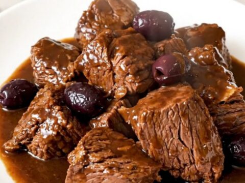 Daube de bœuf brillante et fondante servie dans une assiette blanche avec des olives et de la sarriette.