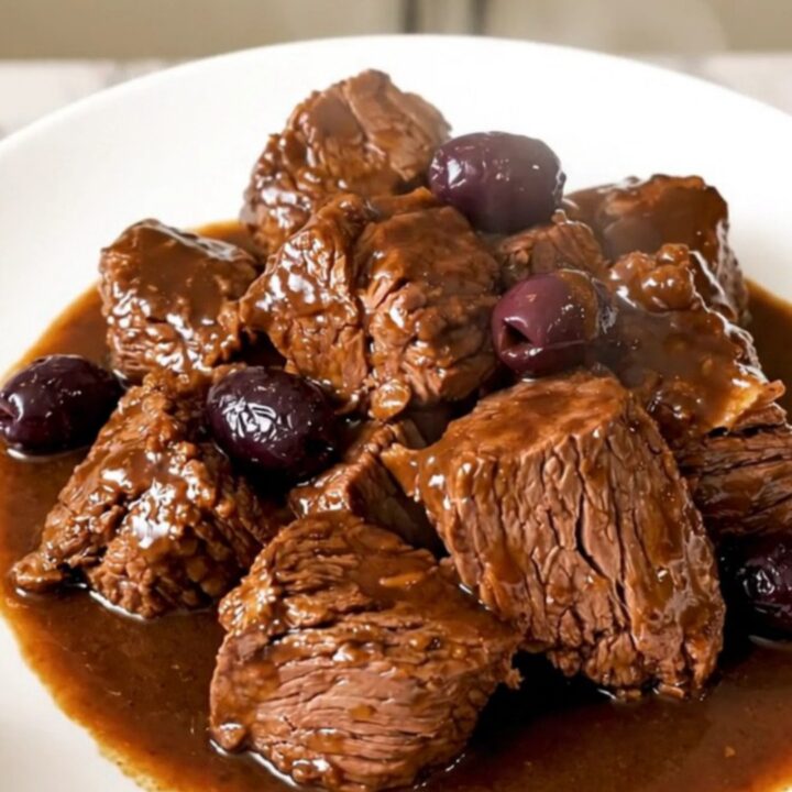 Daube de bœuf brillante et fondante servie dans une assiette blanche avec des olives et de la sarriette.