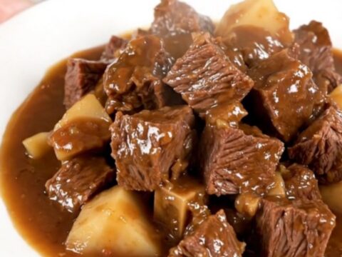 A close-up of a steaming bowl of beef stew featuring tender beef chunks and parsnips in a glossy brown sauce.